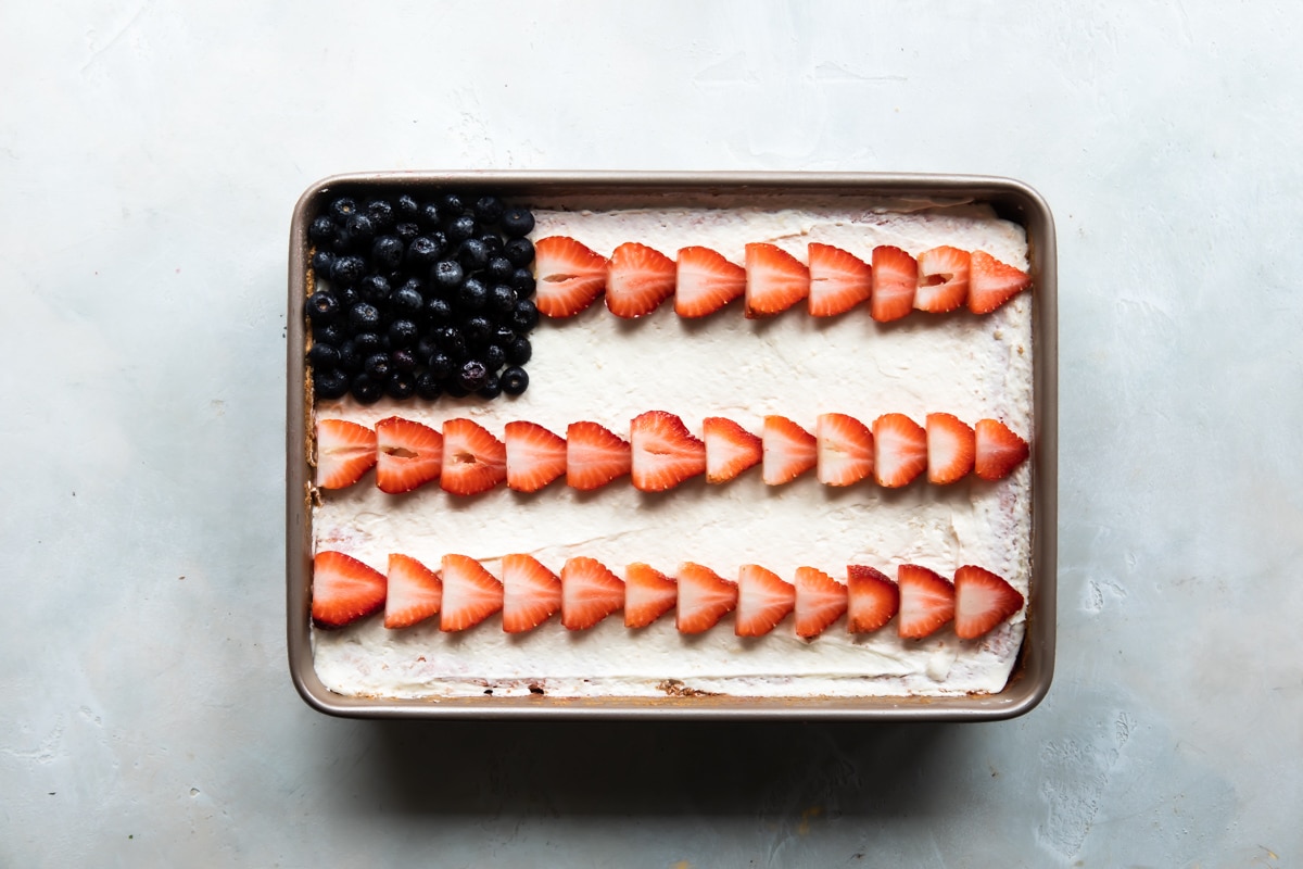 Strawberry jello poke cake topped with strawberries and blueberries to look like an American flag.